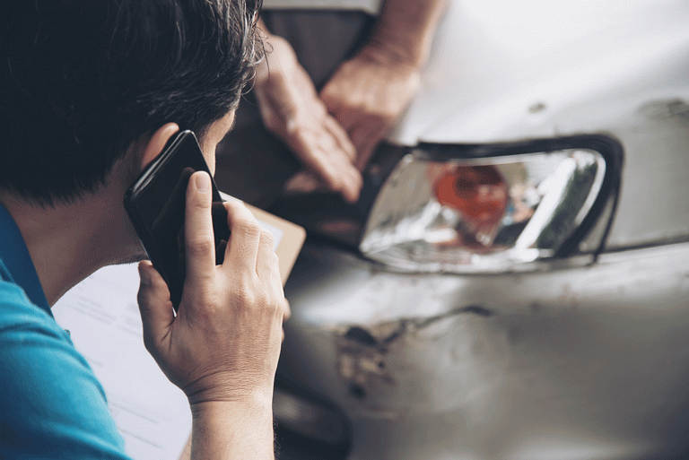 persona revisando su auto y hablando por telefono después de haber tenido un accidente