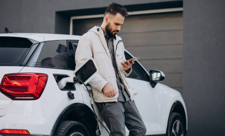 Hombre mirando su celular mientras que su carro está cargando